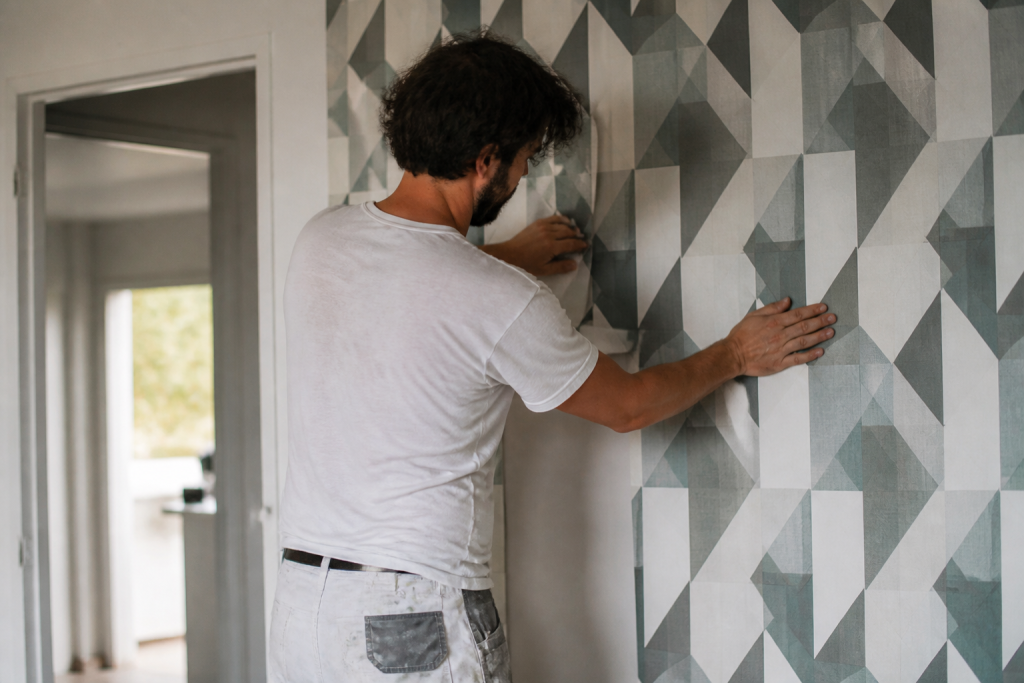 Ouvrier collant papier peint motif geometrique sur mur
