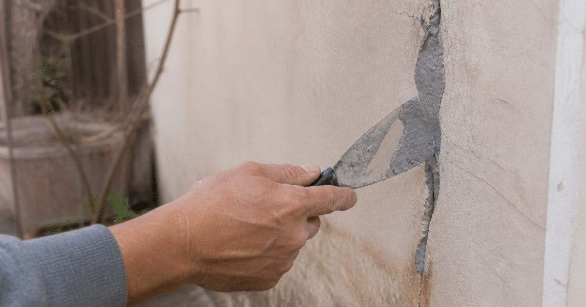 Main appliquant du mastic gris dans une fissure murale verticale
