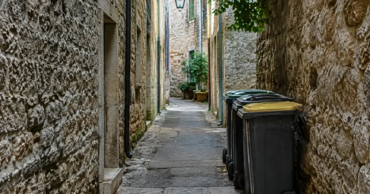 Ruelle etroite bordee de murs en pierre et poubelles